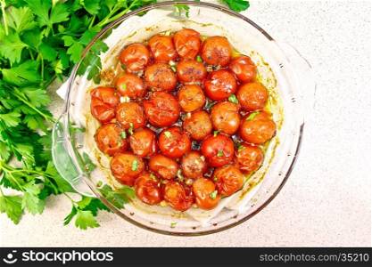 Small tomatoes baked with spices, garlic and salt, parsley in a glass pan on a background of a granite table top