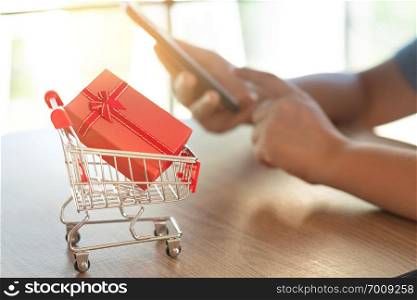 small trolley shopping cart with unrecognized woman shopping online on digital gadget.