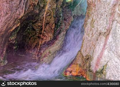 Small waterfall near a hot spring in Main, with colored precipitates of iron, copper, manganese and sulfur compounds, sinter