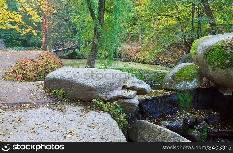 Small waterfall , pond and bridge in autumn park