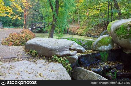 Small waterfall , pond and bridge in autumn park