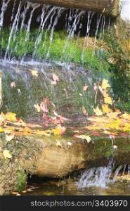 Small waterfall with abscissed yellow leaf and moss in autumn park