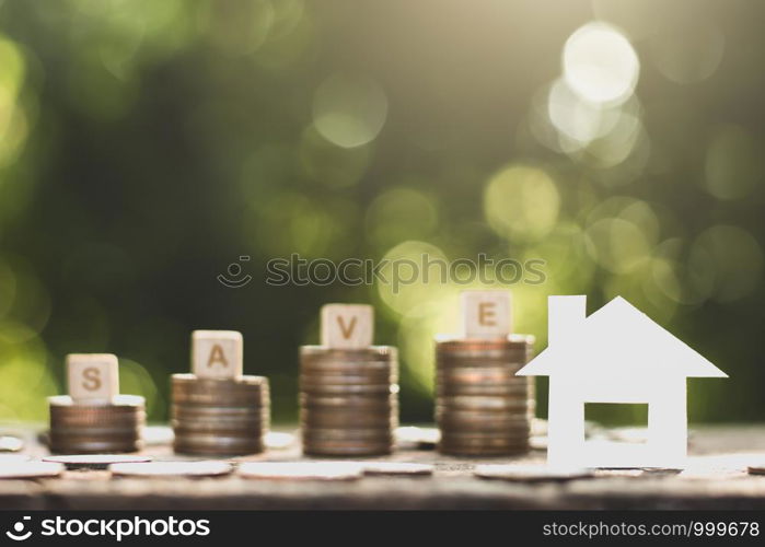 Small white paper houses and coins stacked on old wooden floors, ideas about saving money for the future.