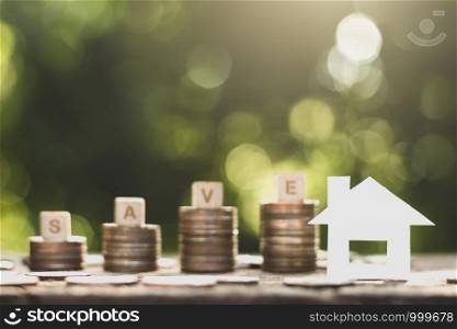 Small white paper houses and coins stacked on old wooden floors, ideas about saving money for the future.
