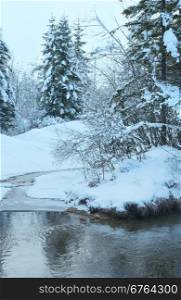 Small winter stream with snowy trees on bank.