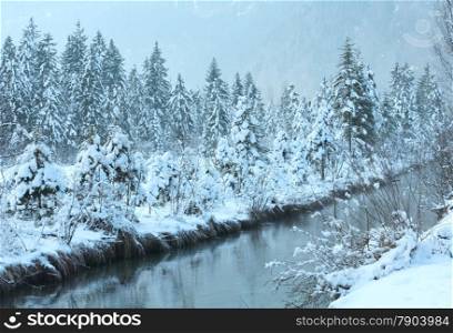 Small winter stream with snowy trees on bank.