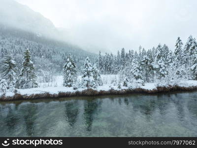 Small winter stream with snowy trees on bank.