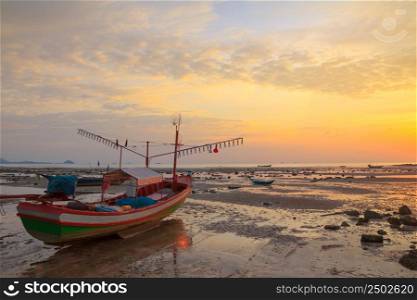 Small wooden boat with light bulbs for night squid fishing on the shore during ebb tide, Thailand