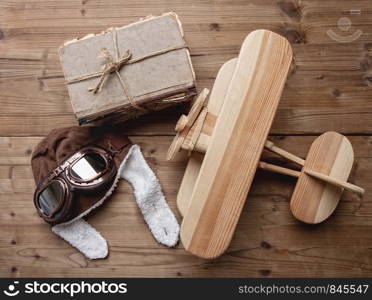 small wooden children's biplane plane on a wooden background next to a pilot helmet and glasses and a stack of old books. old wooden Airplane