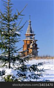 Small wooden church, winter, clear sky at background, green fir tree at foreground, focus at church