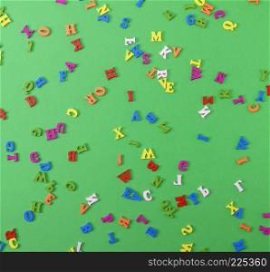 small wooden multi-colored letters of the English alphabet are scattered on a green background, full frame