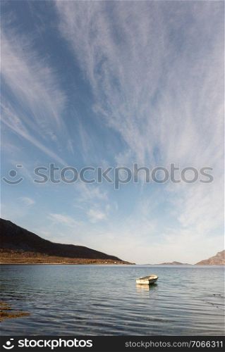 Small wooden rowboat moored in a fjord near Tromso, Norway with rocks in the foreground and distant mountains under a blue sky in a low angle view with ripples on the water