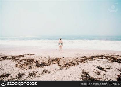 Small young woman in the middle of the beach during a sunny day, mental health concept, solitude