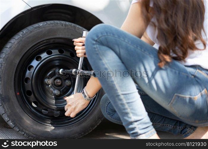 Smart and Attractive Asian woman jacks up her car and uses a wrench to change the wheel on a broken car, uses tools or equipment, tries to solve problems by self, Car Repairing and insurance concept