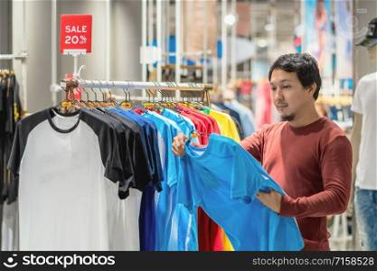 Smart asian man with beard choosing clothes in clothing store at shopping center, looking t-shirts sale 20% off, Fashion and Consumerism Concept.