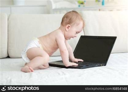 Smart baby in diapers sitting on bed and using laptop