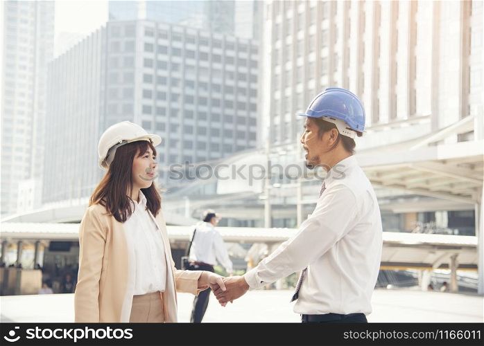 Smart beautiful engineer shaking hands with handsome foreman. background city