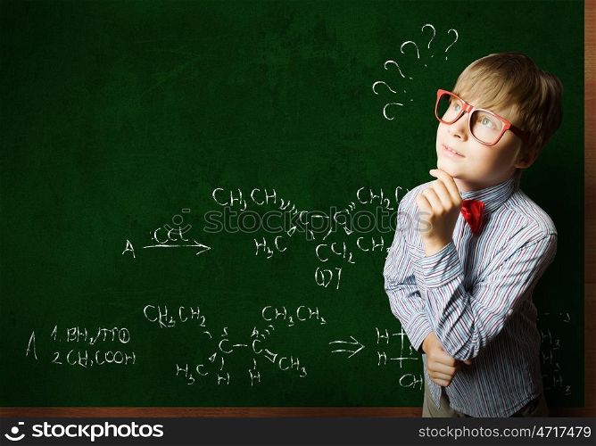 Smart boy in red glasses near blackboard with formulas. Smart schoolboy