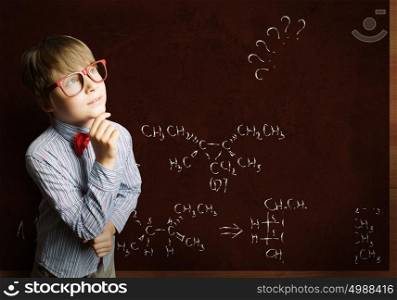 Smart boy in red glasses near blackboard with formulas. Smart schoolboy