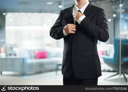 Smart businessman in black suit with adjust the tie pose .