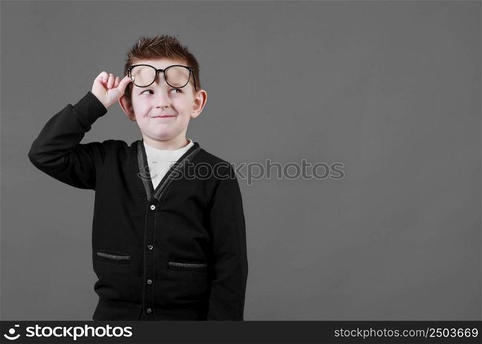 Smart child boy adjusts his glasses and having fun on the grey background, close-up. Studio juvenile portrait in casual clothes. copy space.. Smart child boy adjusts his glasses and having fun on the grey background, close-up. Studio juvenile portrait in casual clothes. copy space