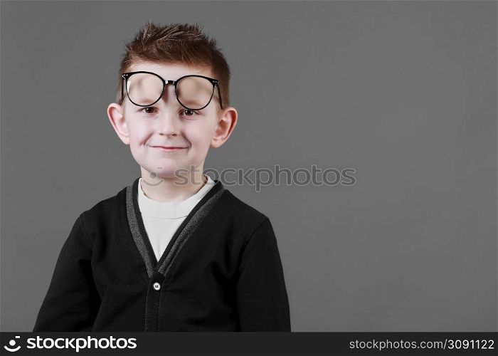Smart child boy adjusts his glasses and having fun on the grey background, close-up. Studio juvenile portrait in casual clothes. copy space.. Smart child boy adjusts his glasses and having fun on the grey background, close-up. Studio juvenile portrait in casual clothes. copy space