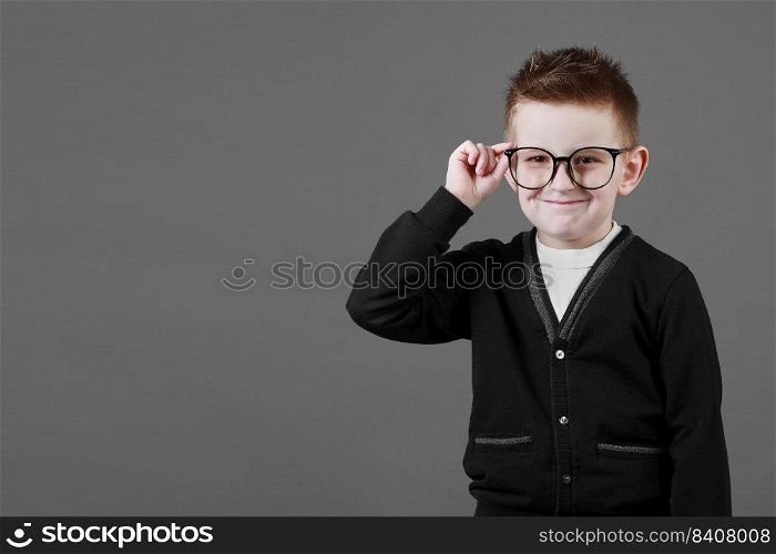 Smart child boy adjusts his glasses with finger on the grey background, close-up. Studio juvenile portrait in casual clothes. copy space.. Smart child boy adjusts his glasses with finger on the grey background, close-up. Studio juvenile portrait in casual clothes. copy space