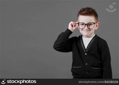Smart child boy adjusts his glasses with finger on the grey background, close-up. Studio juvenile portrait in casual clothes. copy space.. Smart child boy adjusts his glasses with finger on the grey background, close-up. Studio juvenile portrait in casual clothes. copy space