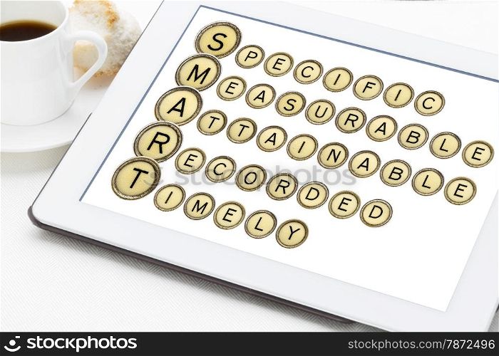 SMART goal setting acronym (specific, measurable,attainable,recorder, timely) in old round typewriter keys on a digital tablet with cup of coffee