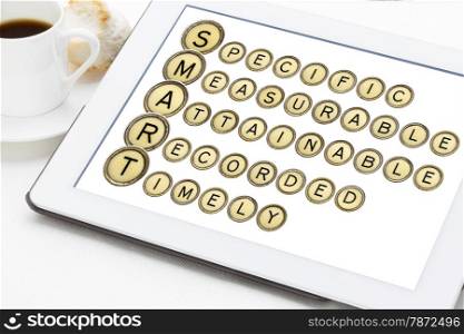 SMART goal setting acronym (specific, measurable,attainable,recorder, timely) in old round typewriter keys on a digital tablet with cup of coffee