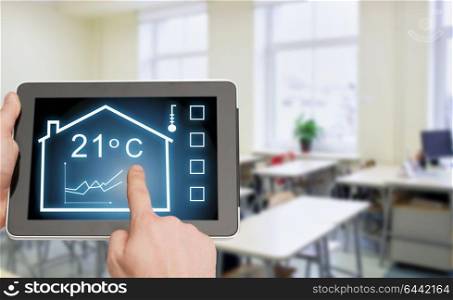 smart home and technology concept - close up of male hands pointing finger to tablet pc computer screen and regulating room temperature over classroom background. tablet pc with smart home settings on screen