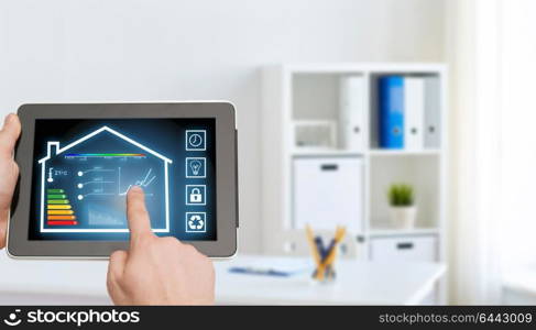 smart home and technology concept - close up of male hands pointing finger to tablet pc computer screen and regulating room temperature over office room background. tablet pc with smart home settings on screen