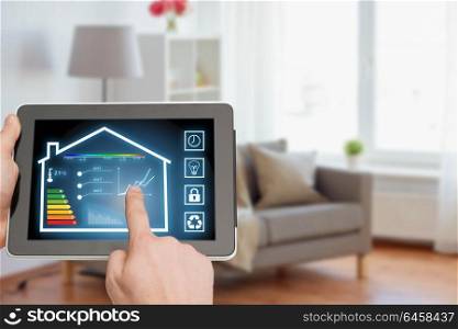smart home and technology concept - close up of male hands pointing finger to tablet pc computer with house settings on screen over living room background. tablet pc with smart home settings on screen