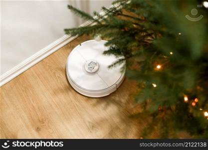 Smart home. Robot vacuum cleaner performs automatic cleaning. Cleans the parquet from Christmas tree needles after the new year. cleans near the Christmas tree after the holidays. Smart home. Robot vacuum cleaner performs automatic cleaning. Cleans the parquet from Christmas tree needles after the new year. cleans near the Christmas tree after the holidays.
