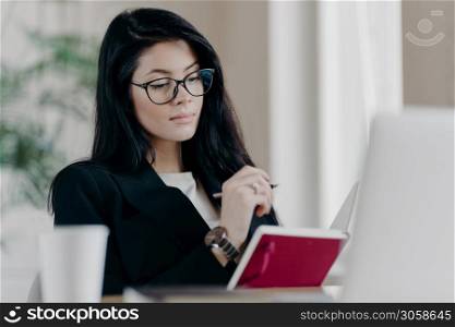 Smart intelligent female teacher in glasses for vision correction learns online courses, makes notes in notepad as watches webinar, works remotely, plans project tasks. People, occupation concept