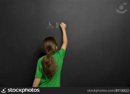 Smart little girl writing in a blackboard, with copy space
