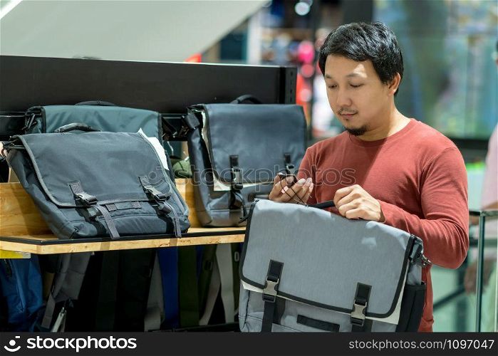 Smart man with beard trying bag and checking the price for make decision in fashion bags shop at shopping mall, Consumerism Concept.