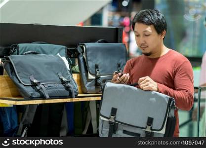 Smart man with beard trying bag and checking the price for make decision in fashion bags shop at shopping mall, Consumerism Concept.