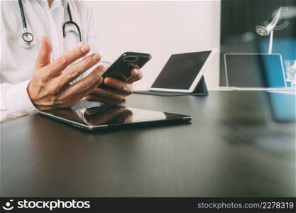 smart medical doctor working with smart phone and digital tablet and laptop computer on drak wooden desk in modern office with glass reflected view