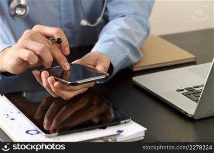 smart medical doctor working with smart phone and stethoscope and laptop and digital tablet computer on dark wooden desk