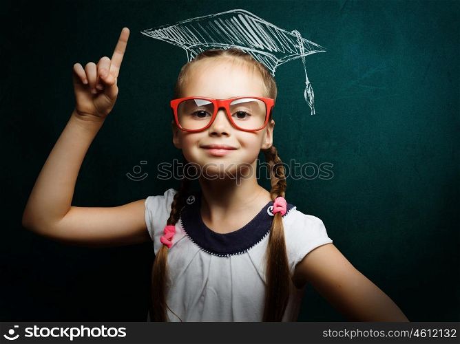 Smart schoolgirl. Genius girl in red glasses near blackboard in master hat