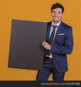 smart smiling young man holding black placard hand against orange backdrop