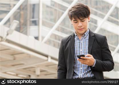 Smart young business man is looking at his mobile phone to check email and news outside office