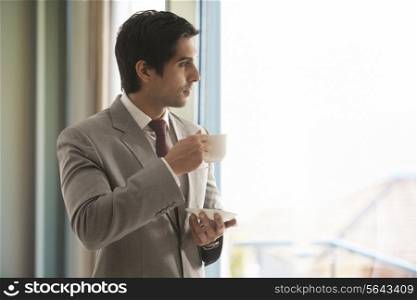 Smart young businessman having cup of tea while thinking