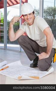 Smart young construction worker smiling with blueprint on floor