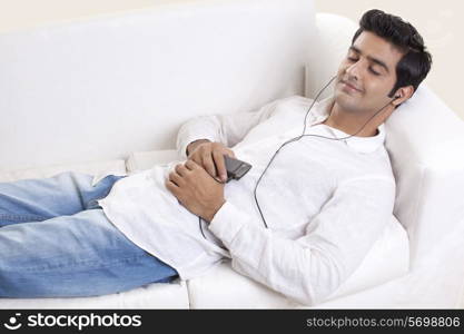 Smart young guy lying on sofa while listening to music