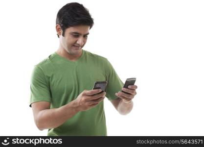 Smart young man text messaging through cell phones over white background