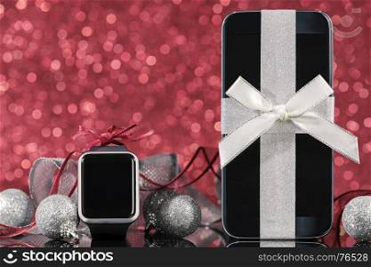 Smartphone and smartwatch and decorations for Christmas tree on black glass table over red background. Focus on smartphone.