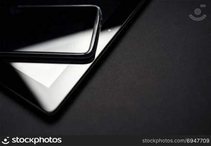 Smartphone Leaning On Tablet close up photo. Electronic devices on black background.