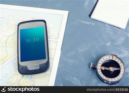 Smartphone, pad, compass on a dark background. Smartphone on a tourist map, compass and notepad